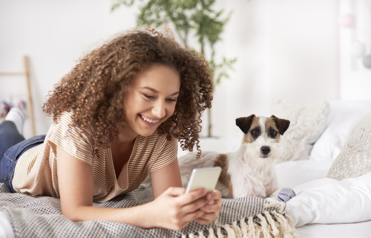 Young woman on phone on bed with dog